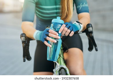 Cropped shot of professional female cyclist holding water bottle, resting, standing with her bike outdoors on a daytime - Powered by Shutterstock