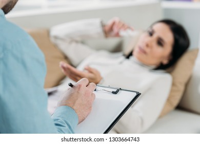 cropped shot of psychotherapist writing on clipboard and young patient in depression lying on couch - Powered by Shutterstock