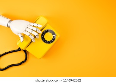 Cropped Shot Of Robotic Hand Reaching For Vintage Phone On Yellow Tabletop