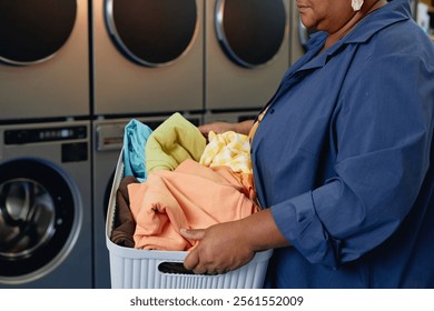 Cropped shot of senior African American woman carrying basket with sorted clothes preparing colored clothes for washing at modern self service laundry room, copy space - Powered by Shutterstock