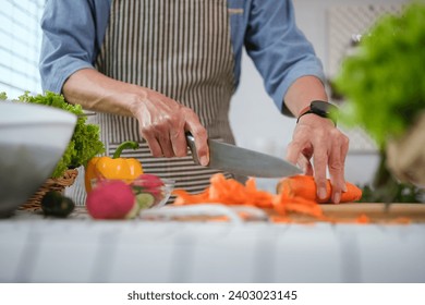 Cropped shot senior man chopping fresh carrot on board preparing a healthy salad in kitchen - Powered by Shutterstock