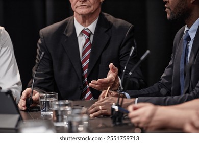 Cropped shot of senior politician in suit talking to colleagues advocating for reforms while sitting at table with other administration officials during committee meeting, copy space