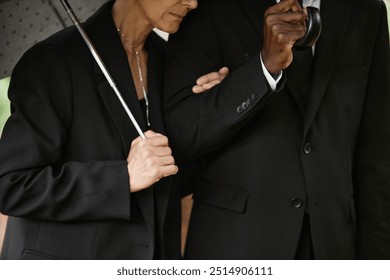 Cropped shot of senior woman in black suit holding husband by arm while hiding from rain under umbrella, copy space - Powered by Shutterstock