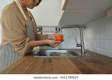 Cropped shot of senior woman hands washing tomato in the kitchen sink before cooking - Powered by Shutterstock