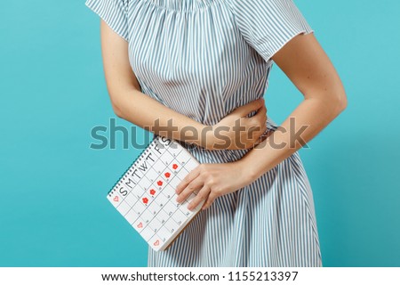 Cropped shot sickness woman in blue dress holding periods calendar for checking menstruation days put hand on tummy isolated on blue background. Medical, healthcare, gynecological concept. Copy space
