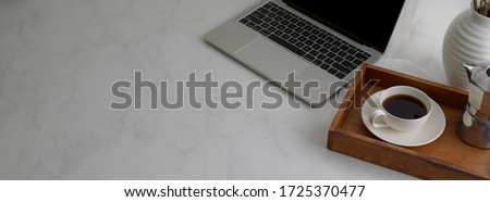 Cropped shot of simple worktable with laptop, coffee cup on wooden tray and copy space on marble desk