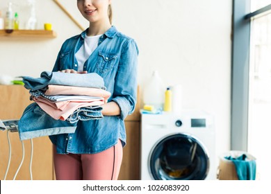 cropped shot of smiling young woman holding stacked clothes at home - Shutterstock ID 1026083920