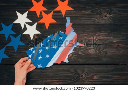 cropped shot of stars and female hand with piece of map with american flag on wooden tabletop, presidents day concept