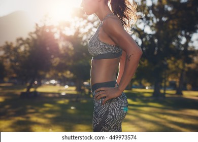 Cropped Shot Of Strong Young Woman Standing With Her Hands On Hips. Strong Woman With Sixpack Abdominals. Fit Female Athlete In Sportswear Standing At A Park.