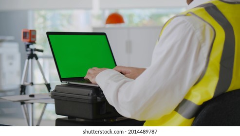 Cropped Shot Of Surveyor Engineer Working On Laptop In Office. Industrial Geodetic Engineer In Reflective Vest Using Computer In Construction Office. Green Screen.