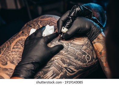 Cropped shot of a tattoo artist hands making an art of a men back with black ink