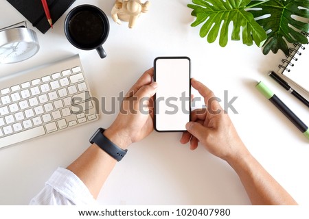 Cropped shot top view of businessman hands using smartphone mockup at the white office desk. Blank screen mobile phone for graphic display montage