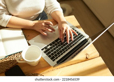 Cropped Shot Top View Of Female Hands Typing On Keyboard Of Opened Laptop At Kitchen Table With White Coffee Mug And Notebook, Studying Online, Checking E-mail, Using Learning Application