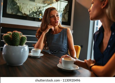 Cropped Shot Of Two Beautiful Young Women Chatting Over A Coffee In A Cafe