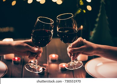 Cropped shot of two women clinking glasses with wine over served table with lit candles