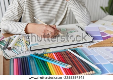 Cropped shot of unknown creative woman draws picture in album engaged in favorite activity develops her painting skills uses colorful crayons poses at table at home. Leisure pastime and hobby concept