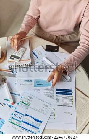 Cropped shot of unknown person calculates energy bill papers manages household budget economical monthly expenditures plans investment surrounded by papers on table. Economy lifestyle concept.