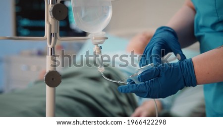 Cropped shot of unrecognizable person in latex gloves injecting poison in drip tube killing senior woman patient in hospital ward. Criminal poisoning old ill female in clinic