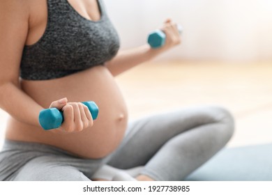 Cropped Shot Of Unrecognizable Pregnant Woman Training With Dumbbells At Home, Expectant Lady In Sportswear Exercising On Fitness Mat In Living Room, Closeup Image With Free Space