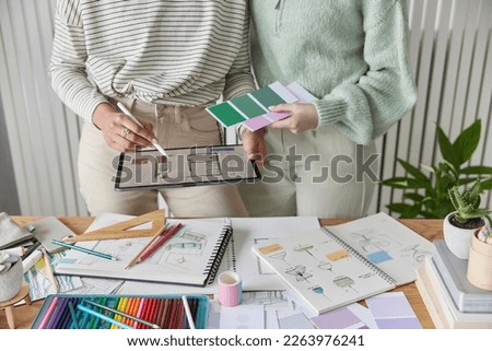 Cropped shot of unrecognizable two interior designers selcts color for room from color swatches palette draw design on digital tablet stand at workplace work as team try to meet client needs