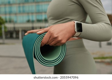 Cropped Shot Of Unrecognizable Woman In Sportswear Carries Rubber Rolled Karemat Prepares For Fitness Training Uses Wearable Smartwatch Going To Practice Yoga. Athletic Female With Sport Facilities