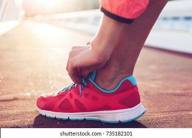 Cropped shot view of fit woman tie shoelaces while standing on asphalt road during jog in summer evening, athletic female tying the laces on running shoes while taking break between training outside - Powered by Shutterstock