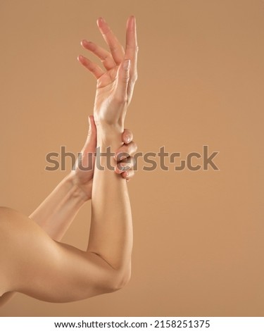 Cropped shot of woman applying cosmetic product on her hands on a beige background. Young woman applying hand cream.