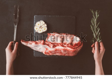 cropped shot of woman with fork and raw ribs slice on stone slate
