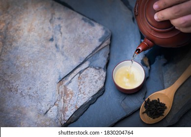 Cropped Shot Of A Woman Hand Pouring Tea From Teapot In Traditional Chinese Teaware. Dark Background With Stone Step Floor.Top Above View. Selective Focus.Copy Space For Text.