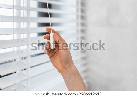 Cropped shot of woman hand pulls the adjustment string closing horizontal window blinds in tradition venetian style made from natural material. Concept of privacy and sunlight protection