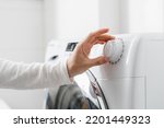 cropped shot of woman hand turn on automatic washing machine or select program with knob on control panel in white bathroom, modern appliances at home