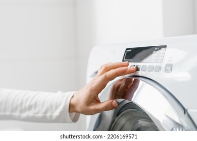 cropped shot of woman hand turn on automatic washing machine or select program with button on control panel in white bathroom in modern house - Shutterstock ID 2206169571