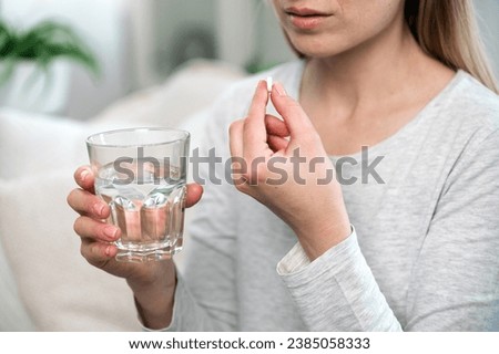 Cropped shot of woman holding white round pill and glass of drinking water, taking vitamins, sedatives, omega 3, supplements for strengthens skin, hair and nails. Beauty and healthcare concept
