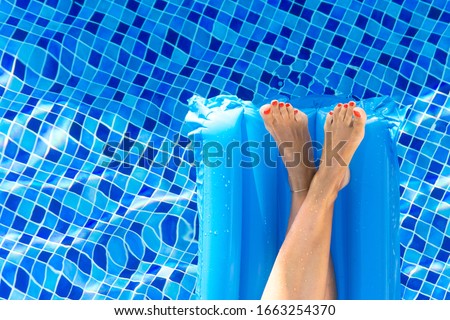 Cropped shot of woman legs on a floating mattress in swimming pool. Female sunbathing on swimming mattress in pool.