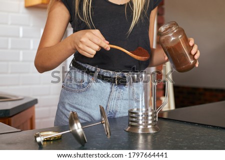 Cropped shot of woman making a cup of coffee while standing behind kitchen counter