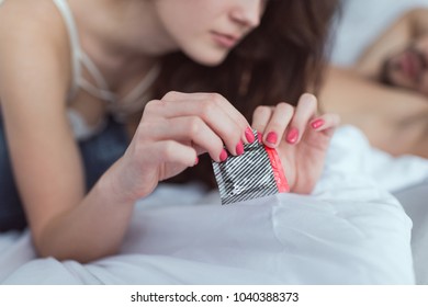 cropped shot of woman opening condom on bed - Powered by Shutterstock