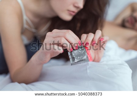 cropped shot of woman opening condom on bed