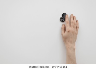 Cropped Shot Of Woman Opening Shutter On Black Round Metal Peephole On Plain White Front Door At Hotel Room Or Home. Security Concept