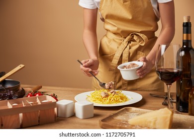 Cropped Shot Of Woman Putting Chicken Meat Onto Spaghetti In Plate On Wooden Table