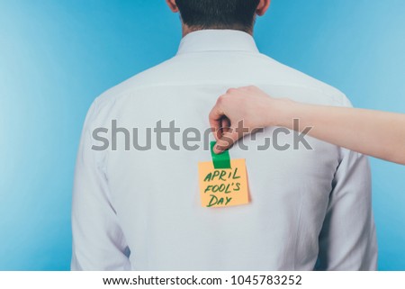 cropped shot of woman putting note with april fools day lettering on males back, april fools day concept