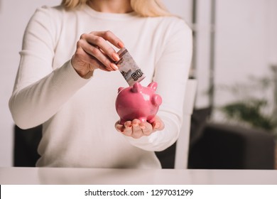 cropped shot of woman putting russian rubles into piggy bank, savings concept 