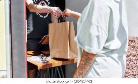 Cropped shot of woman taking paper bag with her order from hands of shop assistant while collecting her purchase from the pickup point. Selective focus. Web Banner - Powered by Shutterstock