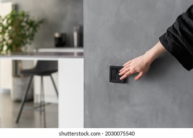 Cropped shot of woman turning light on or off in kitchen using black switch located on grey wall, modern kitchen interior design with plants, furniture and appliances in blurred background - Shutterstock ID 2030075540