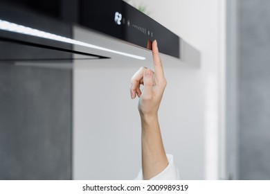 Cropped shot of woman using cooker hood in minimalist modern kitchen with modern integrated appliances, female pressing button on cooking extractor while preparing food at home