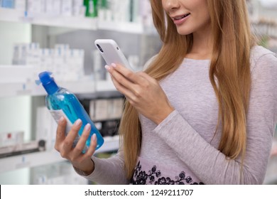 Cropped Shot Of A Woman Using Her Smart Phone, Taking Photo Of A Product She Is Buying At The Drugstore. Female Customer Scanning Label Of Medication Bottle, Shopping At Pharmacy.Online Search Concept