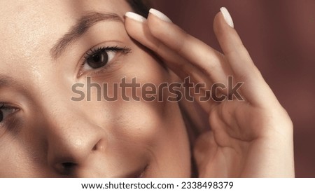Cropped shot of a woman's face in the studio on a pink background close up. A woman touches her eyebrows with her hand. Good vision and eye care. Contact lenses. Cosmetic line for eye contour care.