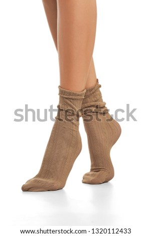 Cropped shot of woman's legs wearing pair of warm beige lace loose socks, standing on tiptoe against the white background. Fashionable leg-wear with stylish ornament. Glamorous legwear for ladies.