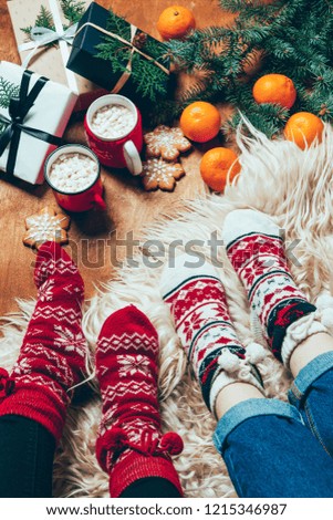 cropped shot of women in winter socks at background with wrapped christmas presents and cups of hot chocolate with marshmallows