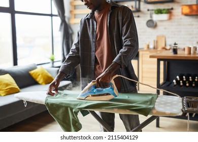 Cropped shot of young African-American man ironing clothes in studio apartment, bachelor lifestyle and household chores concept, copy space - Powered by Shutterstock