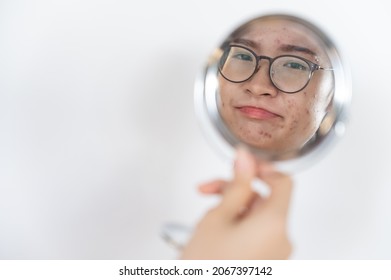 Cropped shot of young Asian woman worried about her face when she saw the problem of acne and scar by the mini mirror. Conceptual shot of Acne and Problem Skin on female face.